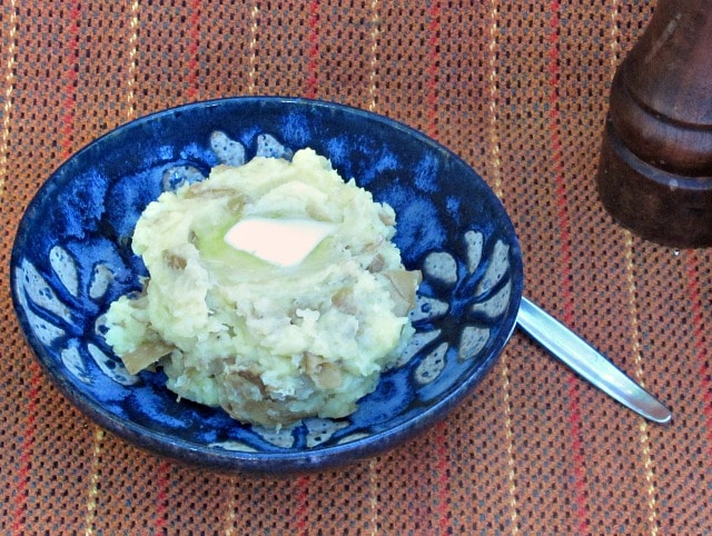 A blue bowl of Mashed Potatoes (With Peel) and a pat of butter