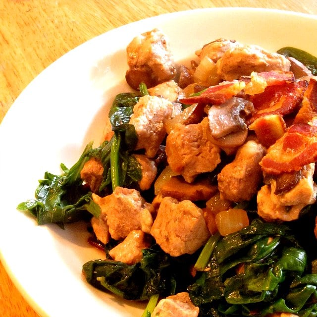 Serving bowl of pork with bacon and mushrooms, and baby greens