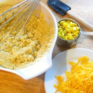 Mixing bowl with cornbread batter, with corn and cheese next to that. 