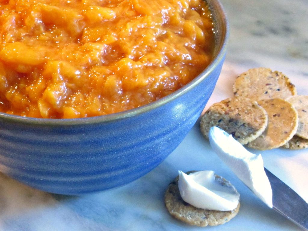 Blue bowl of Peach Sauce, with crackers and cream cheese waiting on the side. 
