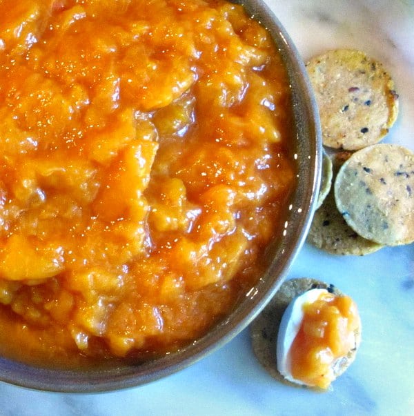 Peach sauce in a bowl, and on a cracker with cheese