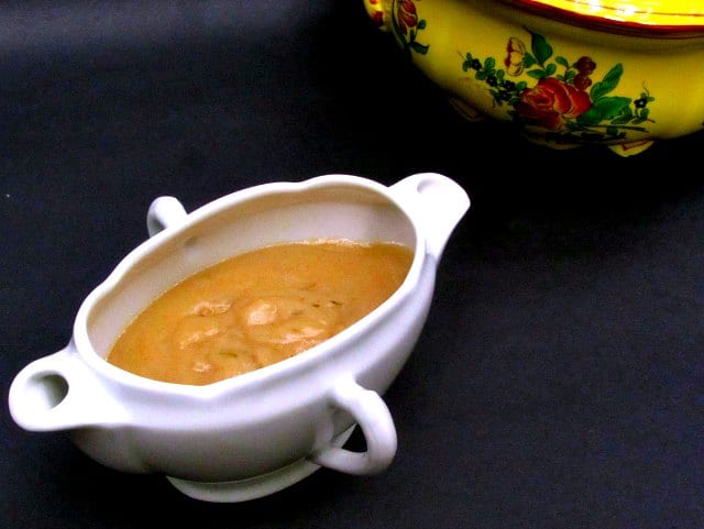 A sauceboat of gluten free chicken gravy next to a serving bowl. 