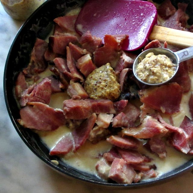 Adding mustard to ham in white sauce.